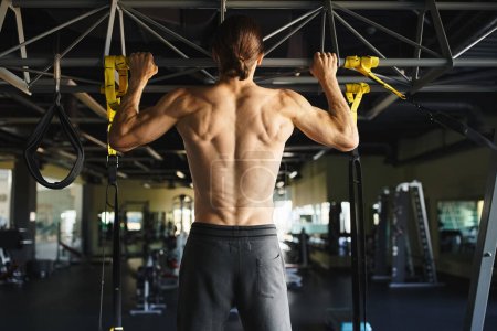 A shirtless man in a gym performs pull ups, showcasing his muscular frame and dedication to fitness.