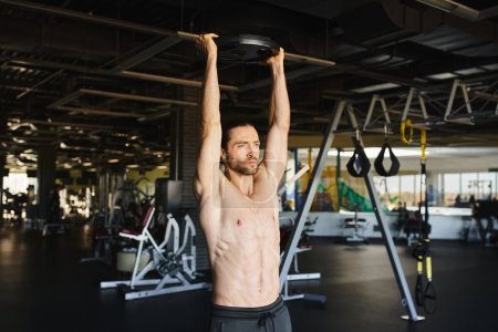Muskulöser Mann ohne Hemd beim Klimmzug im Fitnessstudio.