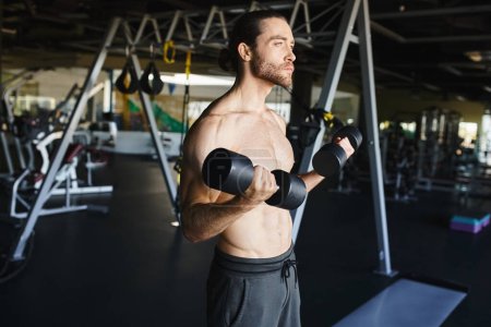 A muscular man in a gym, shirtless, confidently holds two dumbbells, showcasing his dedication to strength training.