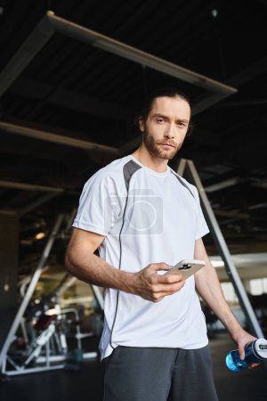Un hombre con una camisa blanca involucrado en su teléfono inteligente después del entrenamiento en el gimnasio
