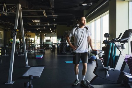 Ein muskulöser Mann steht in einem Fitnessstudio, umgeben von einem Regal mit Trainingsgeräten.