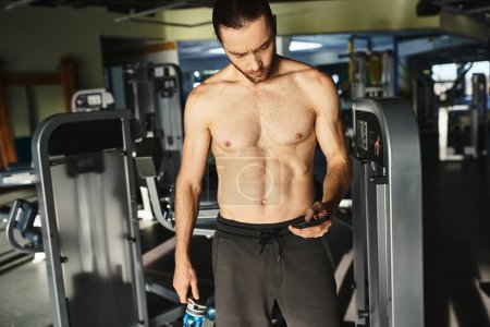 Un homme musclé tenant un téléphone dans une salle de gym, utilisant les médias sociaux après l'entraînement