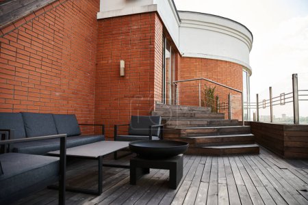 Photo for A serene wooden deck adorned with stylish black furniture sits against a backdrop of a charming brick building - Royalty Free Image