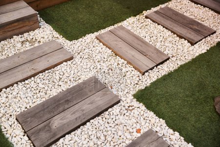 Photo for A serene garden space featuring wooden steps leading down to a gravel pathway surrounded by lush greenery and decorative elements - Royalty Free Image