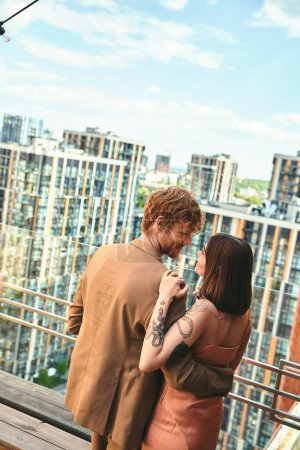 A man and a woman stand together on a balcony, gazing out at the view in contemplation and enjoying each others company