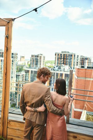 Téléchargez les photos : Un homme et une femme se tiennent tranquillement sur un toit, regardant le vaste paysage urbain en dessous d'eux - en image libre de droit