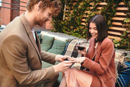 Una alegre pareja durante una propuesta en la azotea, con el hombre ofreciendo un anillo y la mujer radiante.