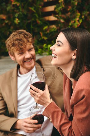 Foto de Un hombre y una mujer se sientan lado a lado, tintineando copas de vino en un gesto romántico - Imagen libre de derechos
