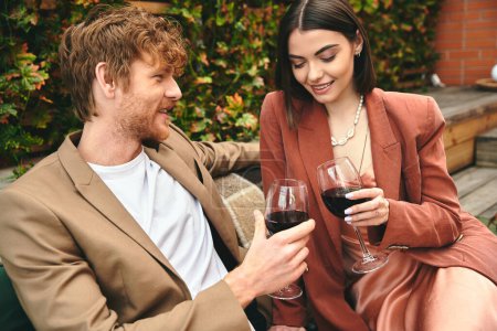 A man and a woman enjoy a romantic moment on a bench, holding wine glasses