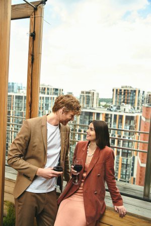 Un hombre con un traje afilado está junto a una mujer sosteniendo una copa de vino, exudando sofisticación y refinamiento en un evento elegante