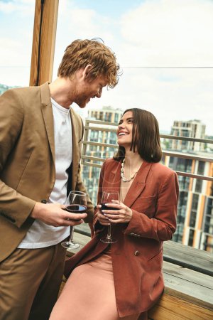 A stylish man stands beside a woman gracefully holding a glass of wine