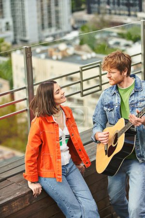Téléchargez les photos : Un homme et une femme se frottent passionnément des guitares sur un balcon, créant ensemble une belle musique sous le ciel ouvert - en image libre de droit