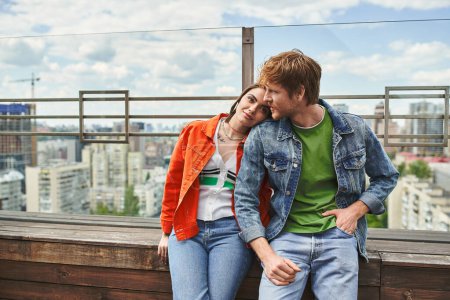 Un homme et une femme sont assis ensemble au sommet d'un bâtiment, surplombant le paysage urbain alors qu'ils partagent un moment d'intimité et de connexion