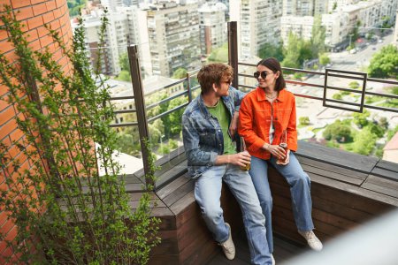 Ein Paar sitzt zusammen auf einem Dach, genießt die Aussicht und die Gesellschaft der anderen vor der Kulisse der Skyline der Stadt