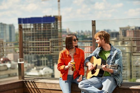 Ein Mann und eine Frau sitzen auf einem Sims, vertieft in Gitarrenspiel, und schaffen eine schöne Harmonie inmitten einer heiteren Kulisse