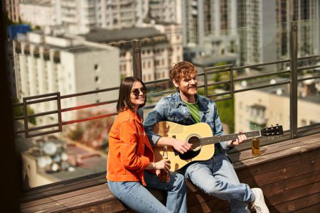 Ein Mann und eine Frau sitzen auf einer Bank, sie hält eine Gitarre, während er aufmerksam zuhört. Sie teilen Melodien unter freiem Himmel