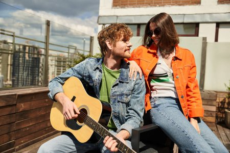 Téléchargez les photos : Un homme assis à côté d'une femme, la sérénade avec une guitare tout en profitant du coucher de soleil ensemble - en image libre de droit