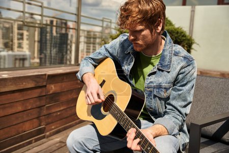 Téléchargez les photos : Un homme talentueux assis sur un banc, jouant passionnément une guitare, perdu dans la musique sous le ciel ouvert - en image libre de droit