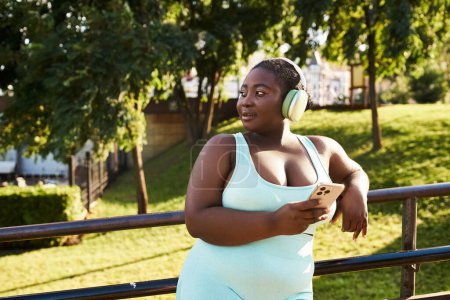 A curvy African American woman in headphones is immersed in music while outdoors.