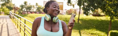 Eine Afroamerikanerin hört freudig Musik auf ihrem Handy, während sie im Freien Kopfhörer trägt.
