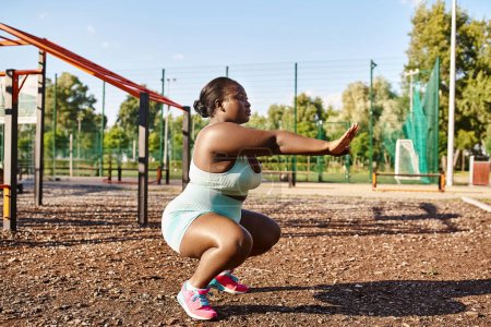 Eine kurvige Afroamerikanerin in Sportbekleidung hockt in einem Park mit einem Spielplatz im Hintergrund.