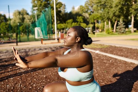 An African American woman in a blue sports bra top stretches her arms outdoors, embracing her body positivity and fitness journey.