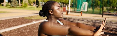 An African American woman in sportswear sits peacefully on a bench in a park, enjoying a moment of relaxation and self-care.