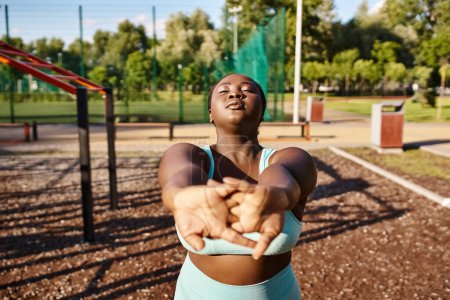 An African American woman in sportswear, showing body positivity, stretching her arms outdoors.