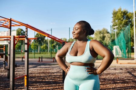An African American woman in sportswear stands confidently in front of a playground, engaging in outdoor exercise.