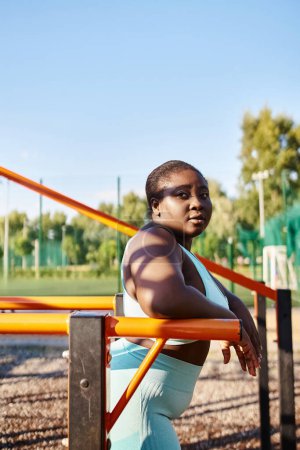 Eine Afroamerikanerin in Sportbekleidung, die Körperpositivität zeigt, sitzt auf einer Parkbank, umgeben von Natur.