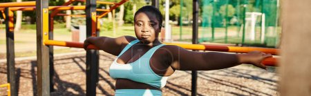 Foto de Una mujer afroamericana en ropa deportiva de pie frente a un patio de recreo, mostrando positividad y fuerza corporal. - Imagen libre de derechos