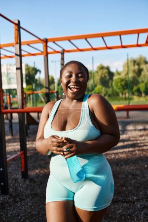 Foto de Una mujer afroamericana en ropa deportiva azul y blanca se para con confianza frente a un parque infantil. - Imagen libre de derechos