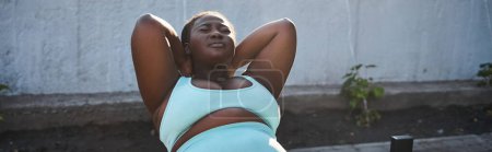 Une femme afro-américaine confiante en vêtements de sport exécute habilement un handstand à l'extérieur, incarnant la positivité du corps.