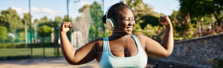 Photo for An African American woman in a sports bra top flexes her muscles confidently outdoors, showcasing body positivity and strength. - Royalty Free Image