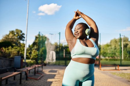 Curvy African American woman in sports bra top stretches her arms outdoors, promoting body positivity and fitness.