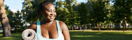 An African American woman, body positive and curvy, holding a yoga mat in a serene park setting.