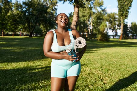 Una mujer afroamericana en un traje azul mostrando positividad corporal mientras sostiene una alfombra deportiva