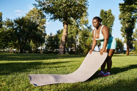 Una mujer afroamericana con curvas en ropa deportiva de pie con confianza junto a una alfombra deportiva