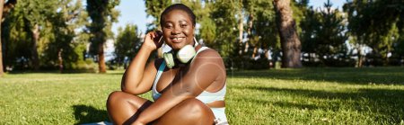Eine kurvige Afroamerikanerin in Sportbekleidung sitzt im Gras und genießt Musik
