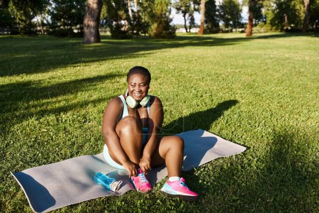 Una mujer afroamericana con curvas en ropa deportiva sentada en una toalla, disfrutando del aire libre en un entorno tranquilo y sereno.