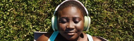 Une jeune fille, avec écouteurs allumés, se trouve dans l'herbe, profitant de la musique et du calme à l'extérieur.