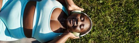 Une femme, avec un chapeau sur la tête, se détend allongée dans l'herbe sous le soleil chaud.