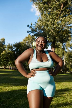 A curvy African American woman in blue sportswear stands gracefully in the lush green grass outdoors.