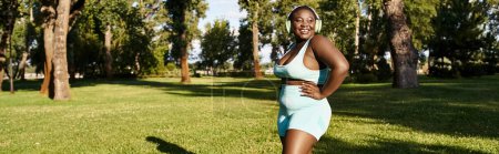 Téléchargez les photos : Une femme afro-américaine, corps positif et élégant, se tient avec confiance sur l'herbe verte luxuriante. - en image libre de droit