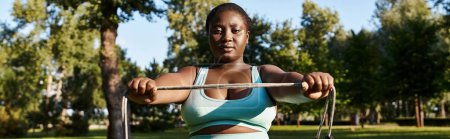 Eine Afroamerikanerin, körperlich positiv und stark, hebt ein Springseil in einer lebendigen Parklandschaft.