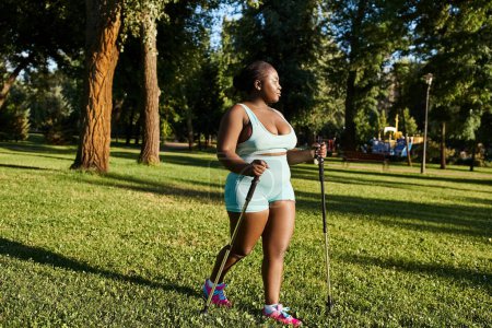 An African American woman in sportswear stands tall in the grass, confidently holding a walking stick.