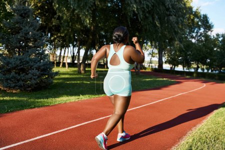 Una mujer afroamericana en ropa deportiva corre por una pista roja, mostrando positividad corporal y atletismo.