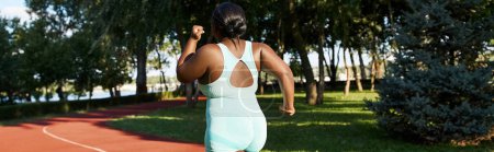 Una mujer afroamericana con curvas en ropa deportiva corre a lo largo de una pista roja en un día soleado