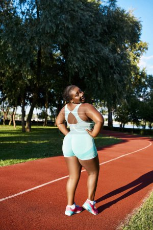 Eine Afroamerikanerin in Sportbekleidung steht selbstbewusst auf einem Tennisplatz, die Hände an den Hüften.