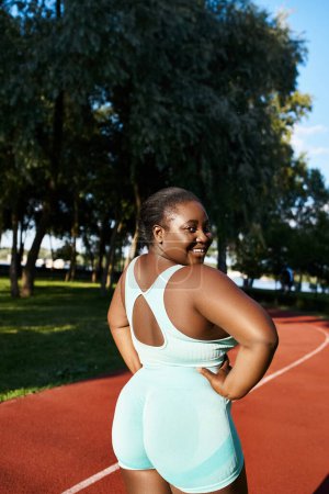 Una mujer afroamericana está de pie con confianza en una cancha, mostrando su atletismo y fuerza.